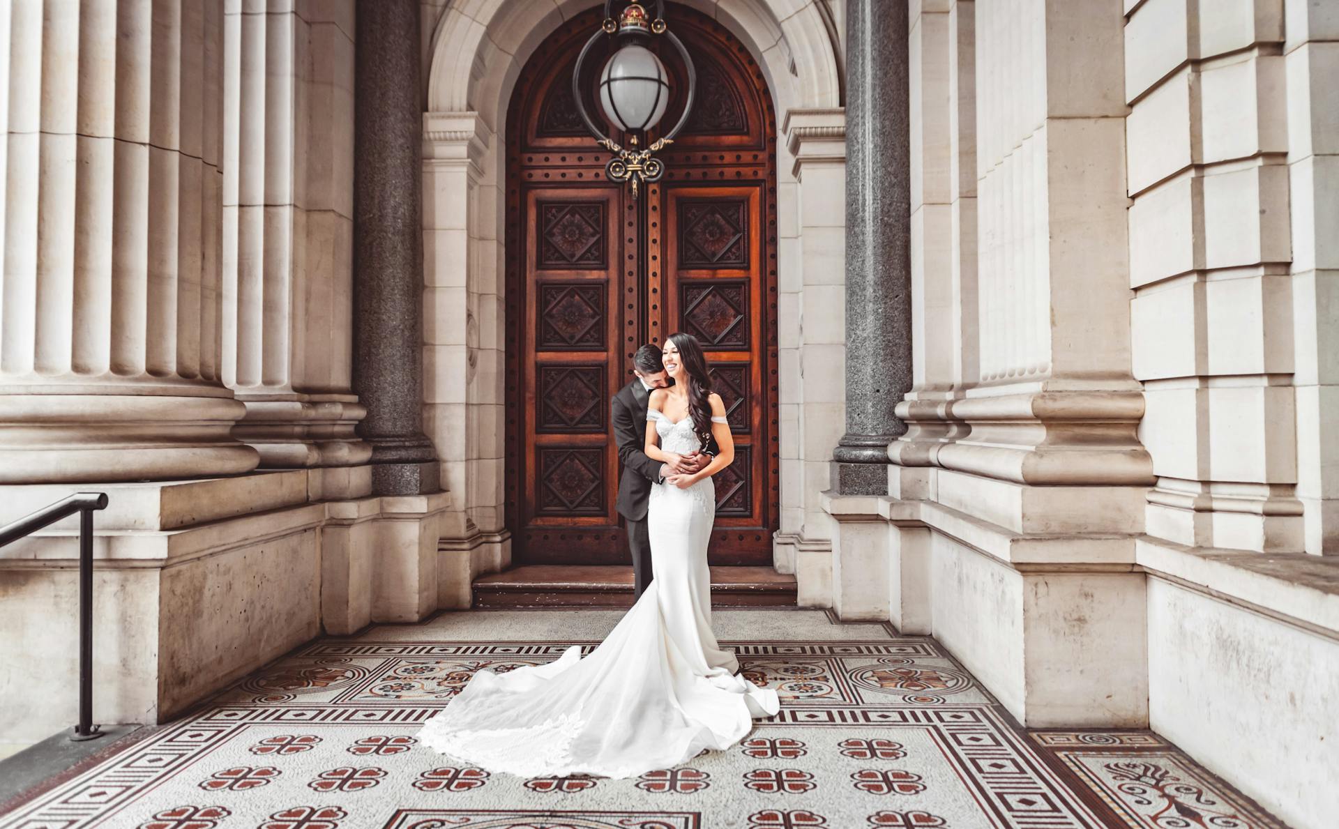 Brautpaar steht in einem edlen Foyer vor roter Tür. 